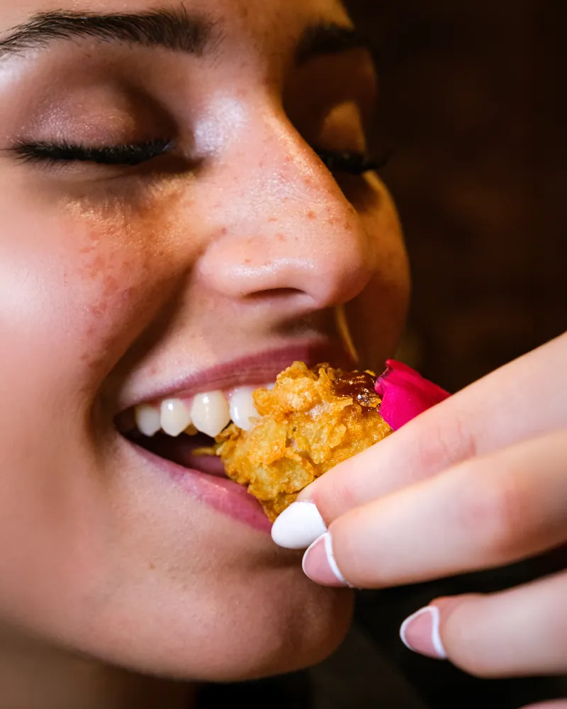 Primo piano di un'ospite sorridente che assaggia un boccone fritto