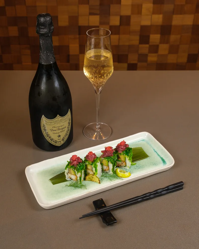 Uramaki con verdure e tartare sulla tavola accanto a bottiglia e calice di champagne